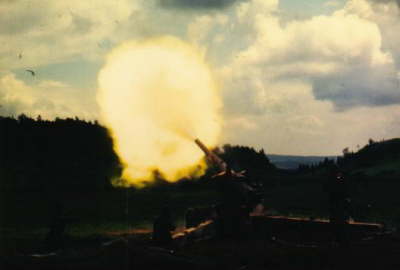 FK 155 feuert. Links oben vor dem Feuerball das Geschoss als kleinerStrich. Der Staub auf dem Geschütz fängt an sich heben.